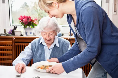 Alte Frau bekommt essen serviert von Betreuerin